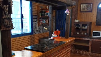 A kitchen with a brick backsplash, wooden countertop, and a window with blue shutters.