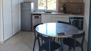 Eine kleine Küche mit einem runden Tisch, Stühlen, einem Kühlschrank, einer Spüle und Holzschränken.