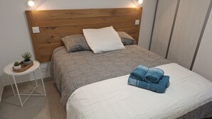 Ein ordentlich bezogenes Bett, ein kleiner Nachttisch mit einer Pflanze und eine wandmontierte Leuchte.