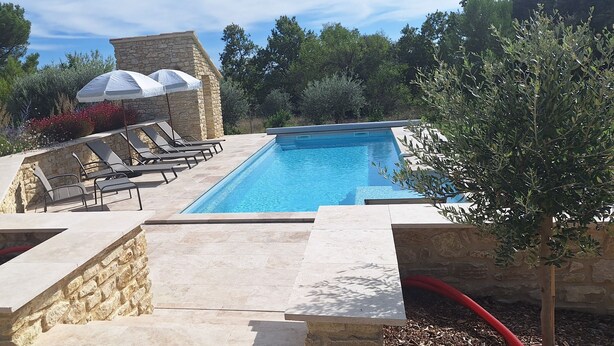 Ein Swimmingpool mit Liegestühlen und Sonnenschirmen, umgeben von Steinmauern und viel Grün.