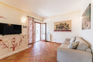 Un soggiorno con televisore, divano, un mobile decorato con un motivo alberello, un quadro e pavimento piastrellato.