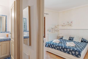 Una camera da letto con un letto, un comodino, un'opera d'arte appesa al muro e un bagno con lavandino e specchio.