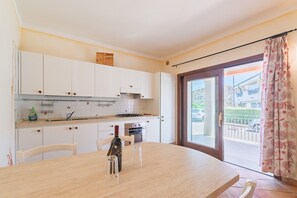 Una cucina con mobili bianchi, un tavolo da pranzo, sedie, una bottiglia e un bicchiere.