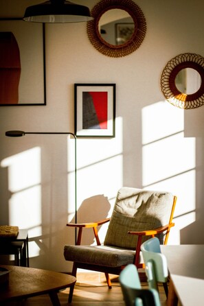 Ein Zimmer mit einem Sessel, einem Tisch, einem gerahmten Bild und einem Spiegel an der Wand.