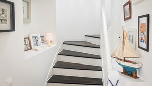Tummanvärisillä porrasaskelmilla varustetut portaat, pieni laivamalli ja seinillä olevat kehystetyt valokuvat.