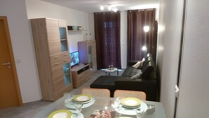 Kompakti olohuone, jossa on ruokailutila, sohva, televisio ja puinen kaappi.