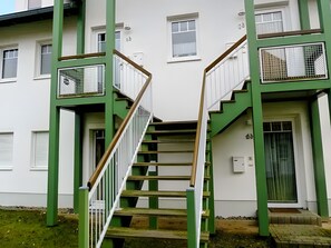 Ein Gebäude mit einer Treppe, die zu einer Tür führt, umgeben von grün gestrichenen Säulen und weißen Wänden.