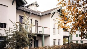 Monikerroksinen rakennus, jossa on parveke, katettu sisäänkäynti ja etualalla pensasaita.