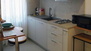 A compact kitchen with a sink, stove, microwave, and a small dining area with a table and chairs. - Dosana Blu Studio 'Aqua Alta' with Wi-Fi and Air Conditioning (Chioggia)