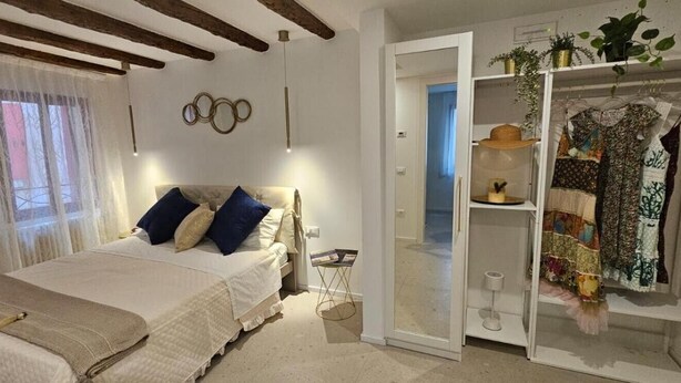 A bedroom with a bed, a wardrobe, a mirror, and a door leading to another room. - Dosana Blu Studio 'Aqua Alta' with Wi-Fi and Air Conditioning (Chioggia)