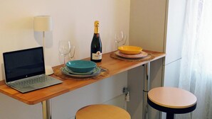 A small dining area with a laptop, a bottle of champagne, and two bowls on a wooden table. - Dosana Blu Studio 'Aqua Alta' with Wi-Fi and Air Conditioning (Chioggia)