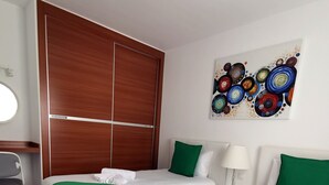 Ett hotellrum med två sängar, ett skrivbord, en stol, en tavla på väggen och en garderob i trä.