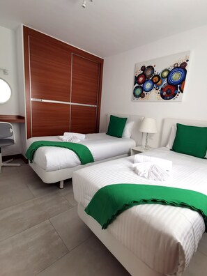 A hotel room with two beds, a desk, a chair, a wall art piece, and a wooden wardrobe. - Holiday Home “Cactus” with Sea View, Wi-Fi and Air Conditioning (Yaiza)