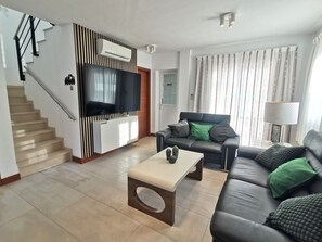 Ein modernes Wohnzimmer mit Flachbildfernseher, einer Couch, einem Couchtisch und einer Treppe.