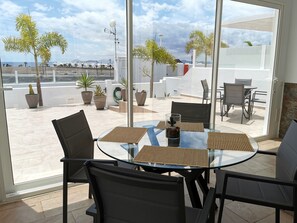 Ein Tisch mit Glasplatte, Stühle, Zimmerpflanzen und Blick auf den Strand.