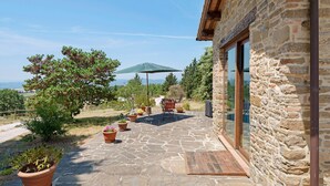 Un bâtiment en pierre doté d’un patio, de plantes en pot, d’une terrasse en bois et offrant une vue sur le paysage.
