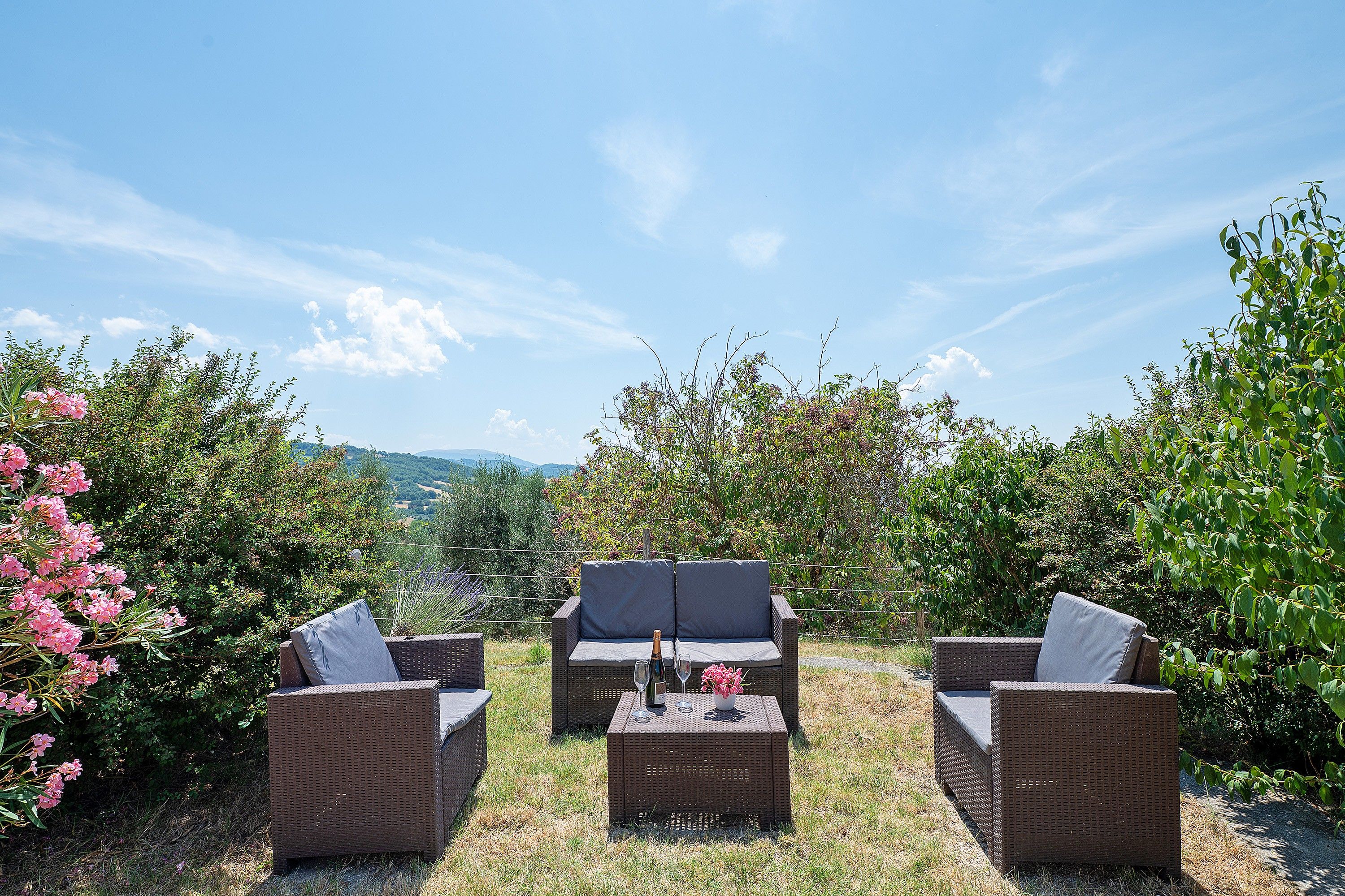 A wicker outdoor seating area with a table, two chairs, and a bottle of champagne.