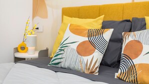 A bed with a patterned headboard, a bedside table with a lamp, and a wall with abstract art. - Neg Naumachia Rooms - Quadruple Room N1 (Catania)