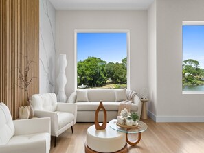 Ein modernes Wohnzimmer mit einer Couch, Sesseln, einem Glastisch und Blick auf einen See und Bäume.