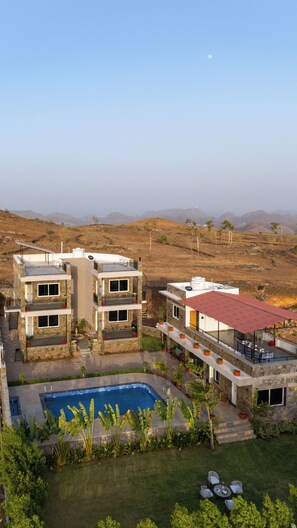 A multi-story building with a swimming pool, outdoor seating, and a view of the surrounding landscape. - Alaya Stays The monolith 4 BHK Villa (Kundal Ubeshwarji)
