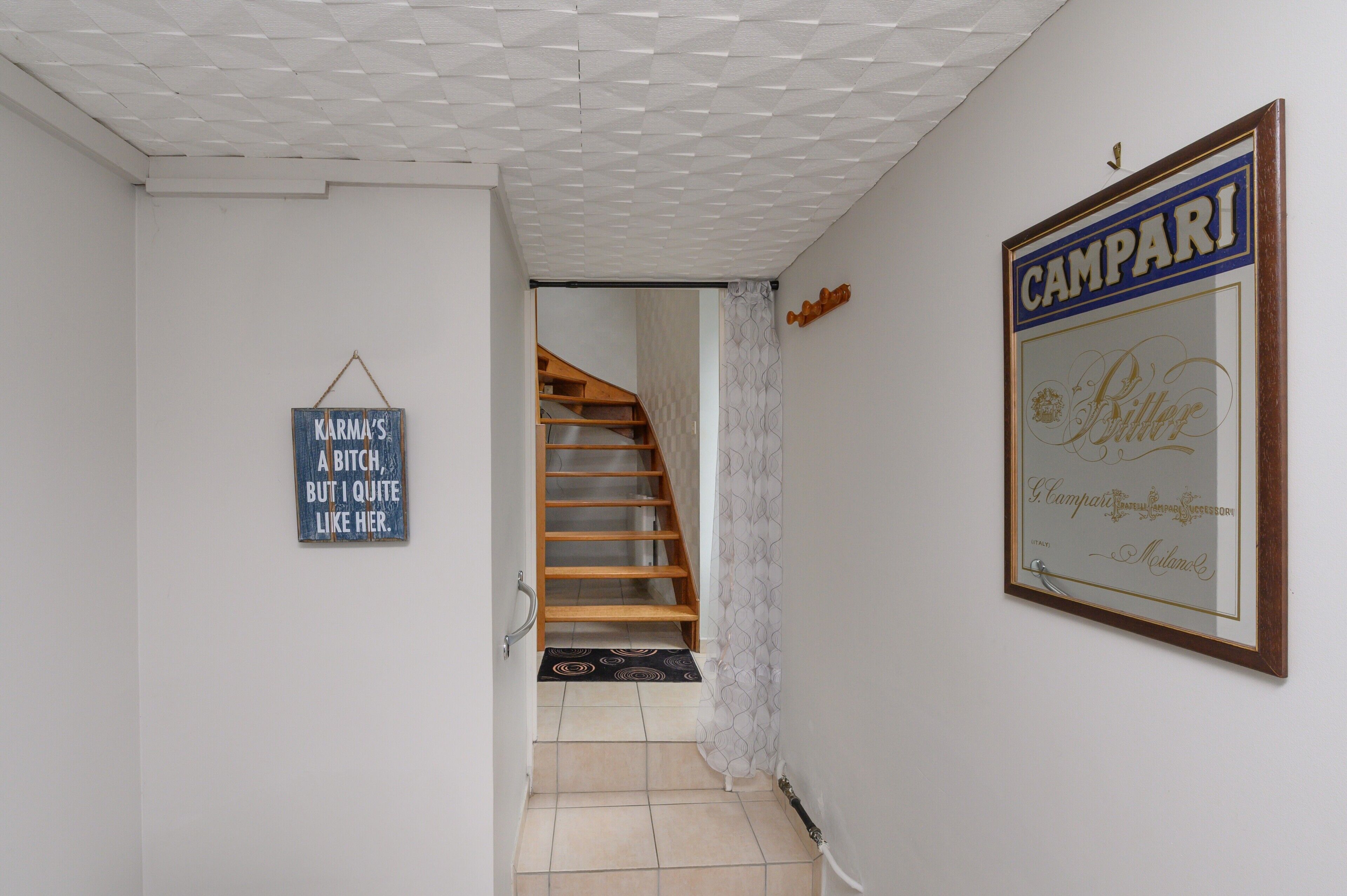 A hallway with a wooden staircase, a framed sign on the wall, and a patterned rug.