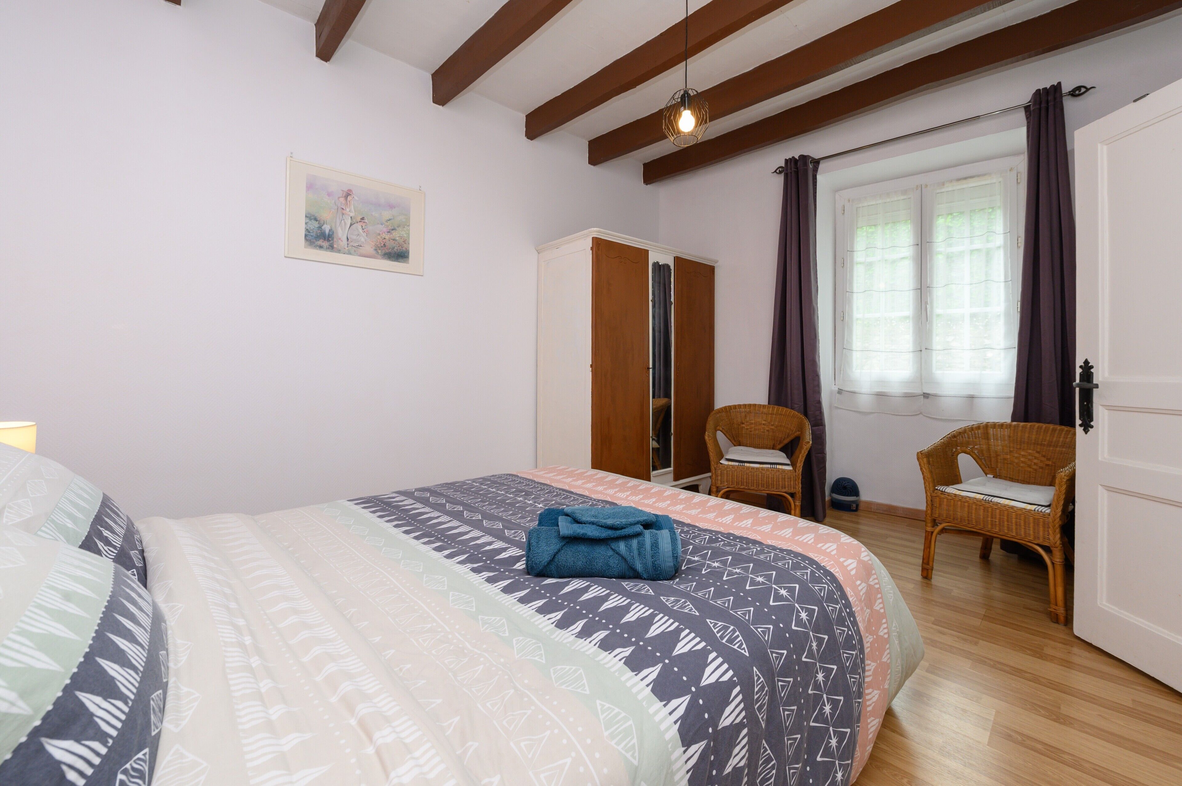 A bedroom with a bed, a wardrobe, a chair, and a window with curtains.