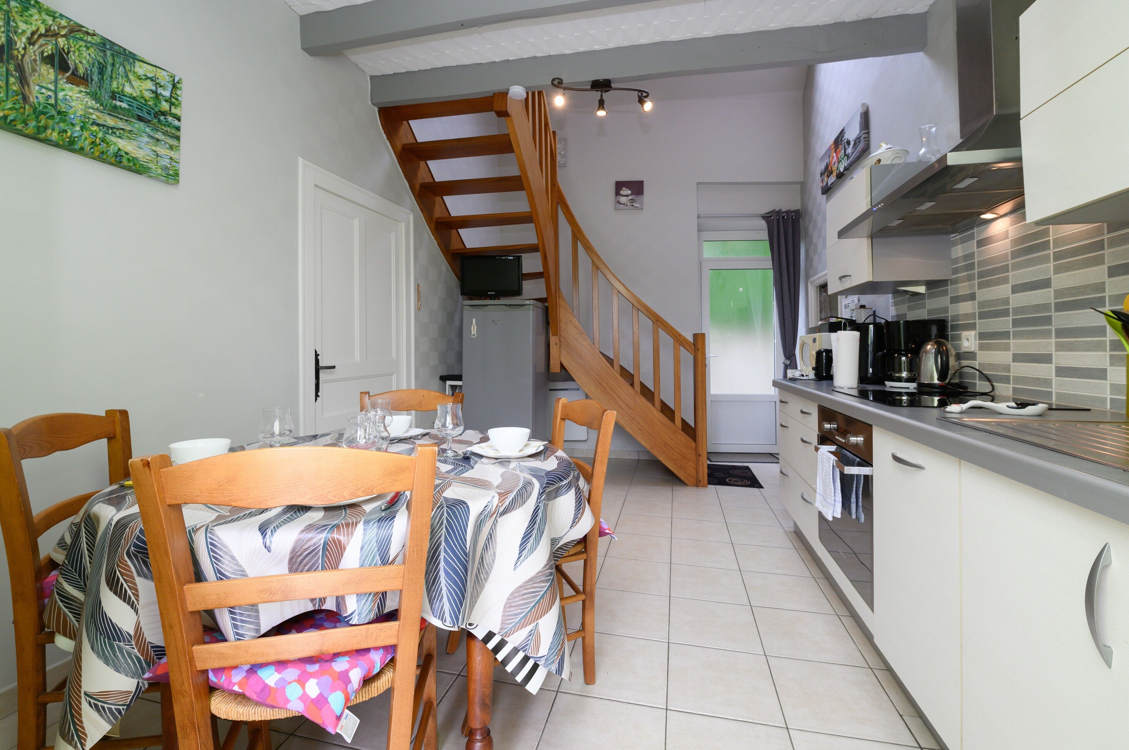 A dining area with a table set for four, a kitchen with modern appliances, and a staircase leading to another level.