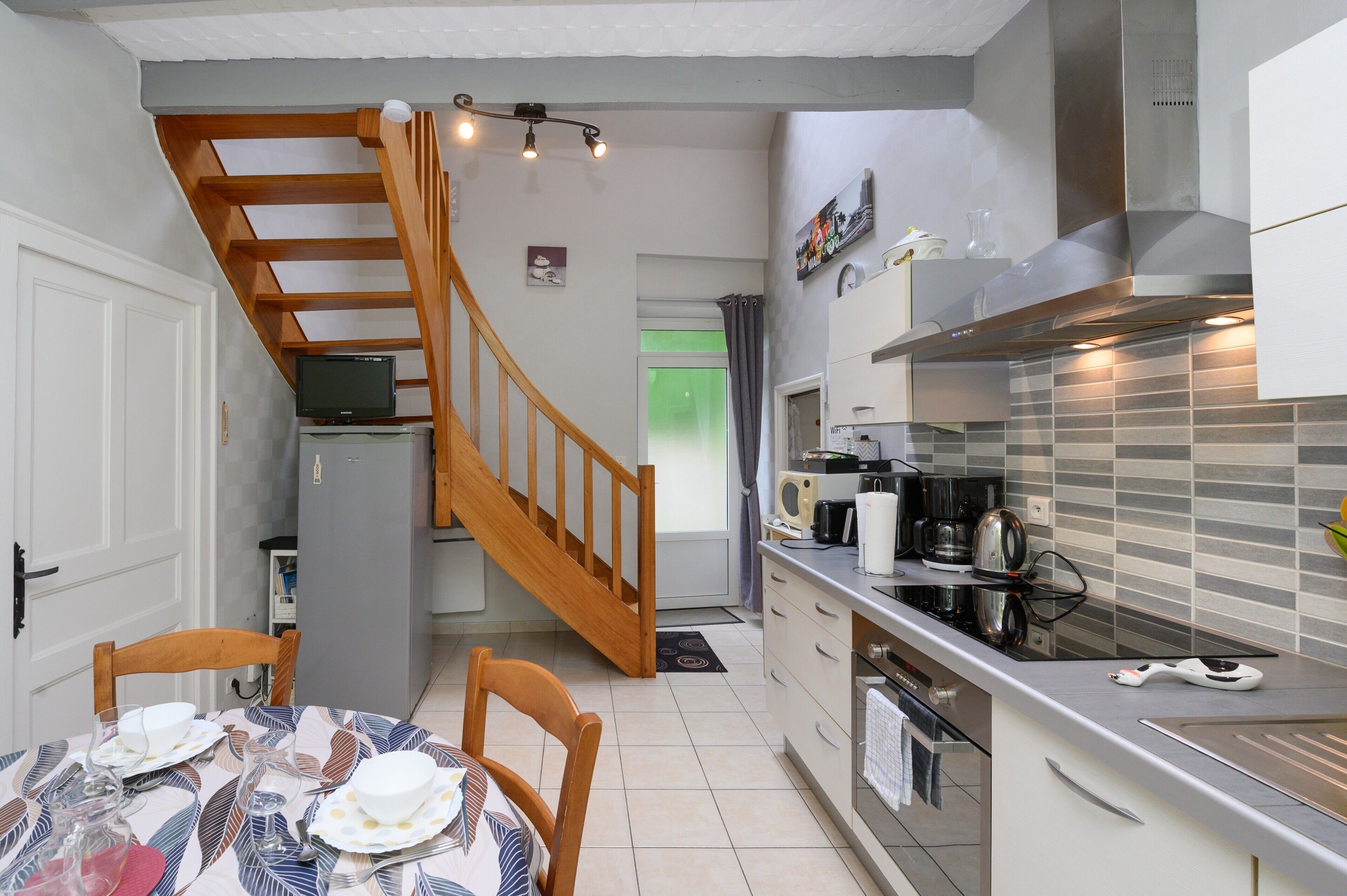A kitchen with a wooden staircase, a dining table set with plates and glasses, and a modern stove.
