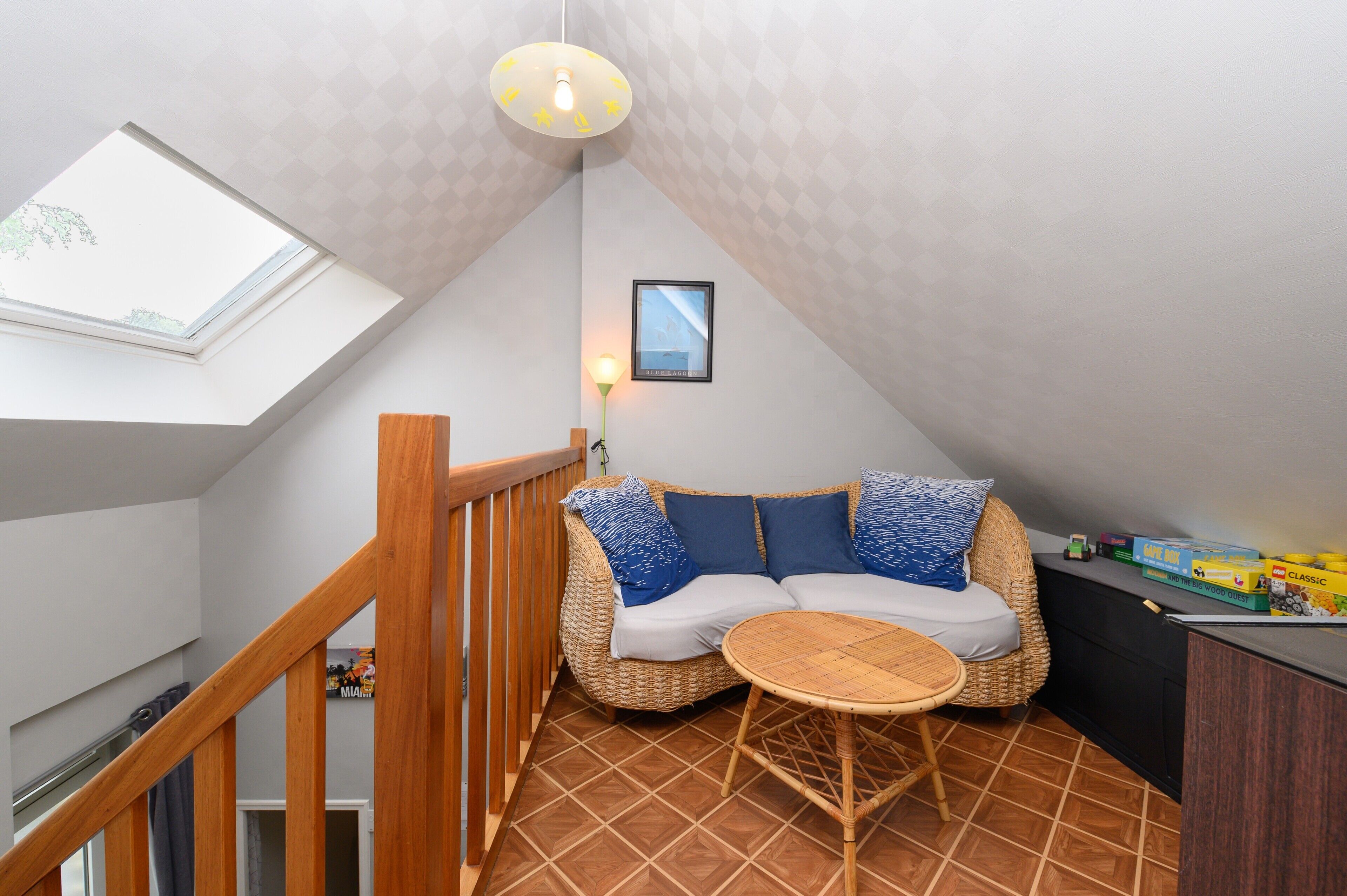 A cozy loft bedroom with a sloped ceiling, a built-in sofa, a small round table, and a view through a skylight.