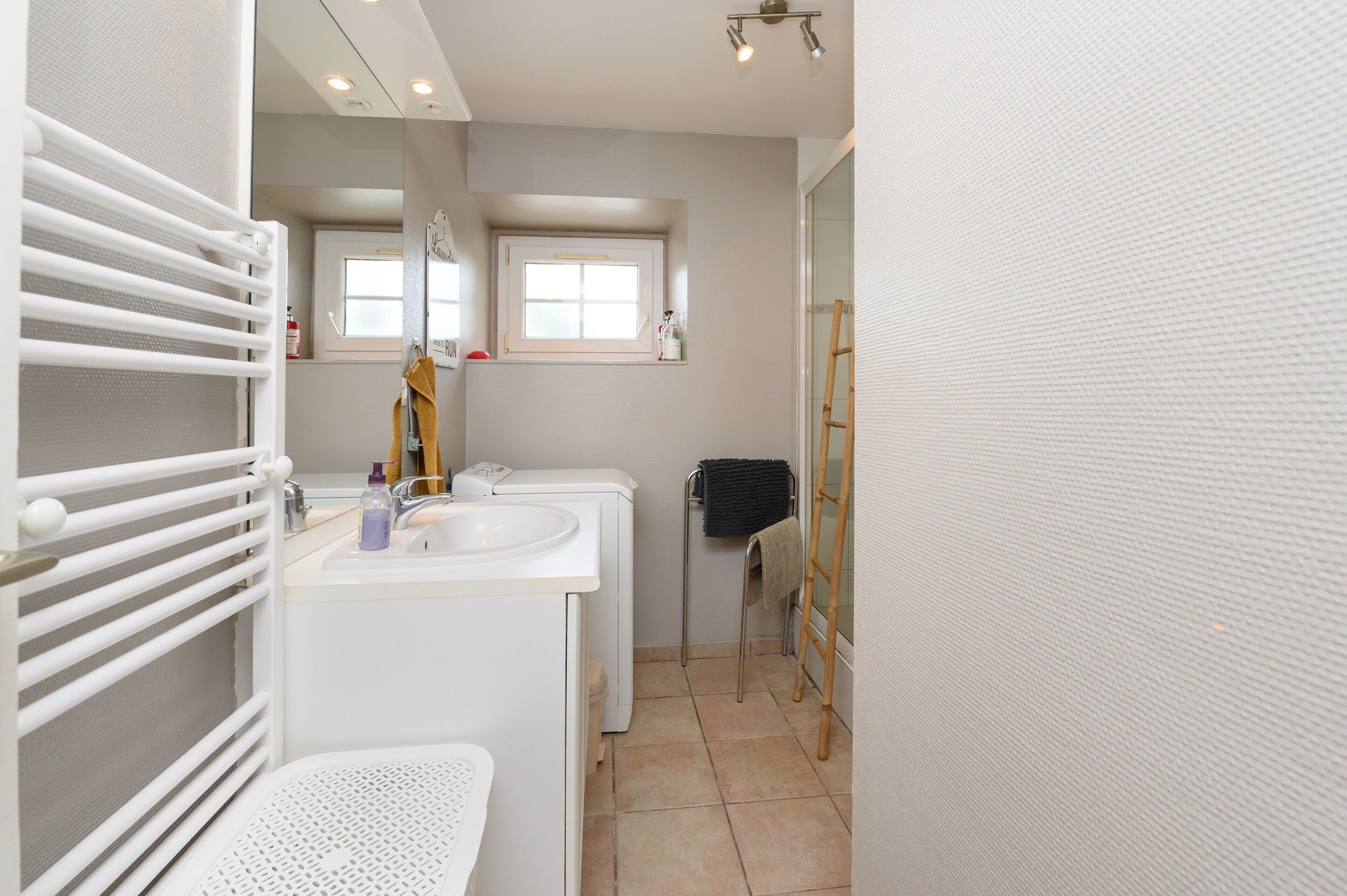 A bathroom with a white sink, mirror, towel rack, and a window.