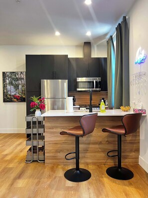 Cozinha moderna com armários escuros, eletrodomésticos de aço inoxidável e um espaço de bar com dois bancos.