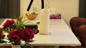 En hotellreception med en neonreklamskylt formad som en våg, ett vinställ i glas, en vas med röda blommor och en svart kran.