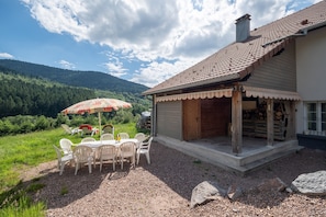 A rustic house with a patio, outdoor seating, and a view of a forested mountain.