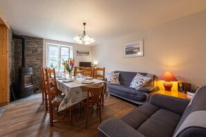 Una sala acogedora con chimenea, una mesa de comedor lista para cuatro personas, un sofá y una lámpara.