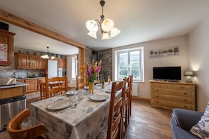 A kitchen with wooden cabinets, a dining table set with plates and cutlery, a chandelier, and a TV on a wooden dresser.