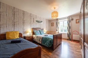 A bedroom with two beds, wooden flooring, a hanging light fixture, and a window with curtains.