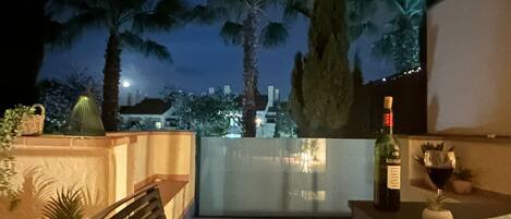 Un balcón con vista a palmeras y al paisaje urbano de noche.