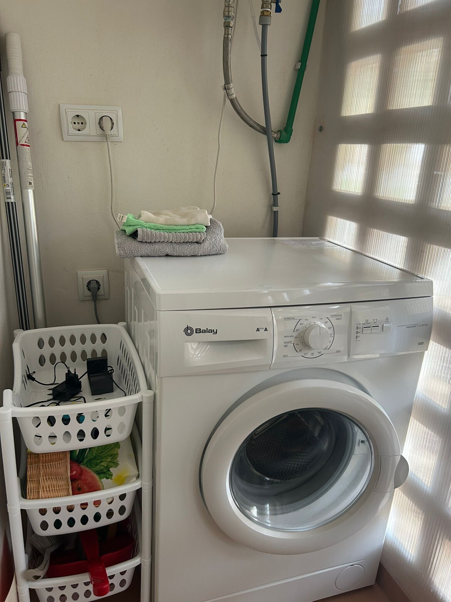 Eine Waschmaschine mit Frontöffnung, einem Bedienfeld, einer Steckdose und einem Schlauch an der Wand.