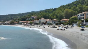 A beach with buildings, umbrellas, and people.