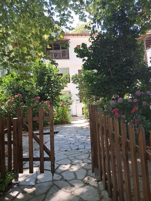 A stone pathway leading to a building with a balcony, surrounded by lush greenery and flowering plants. - Paradise in Ai Giannis Apartment with Sea View, Wi-Fi, and Air Conditioning (Agios Ioannis)