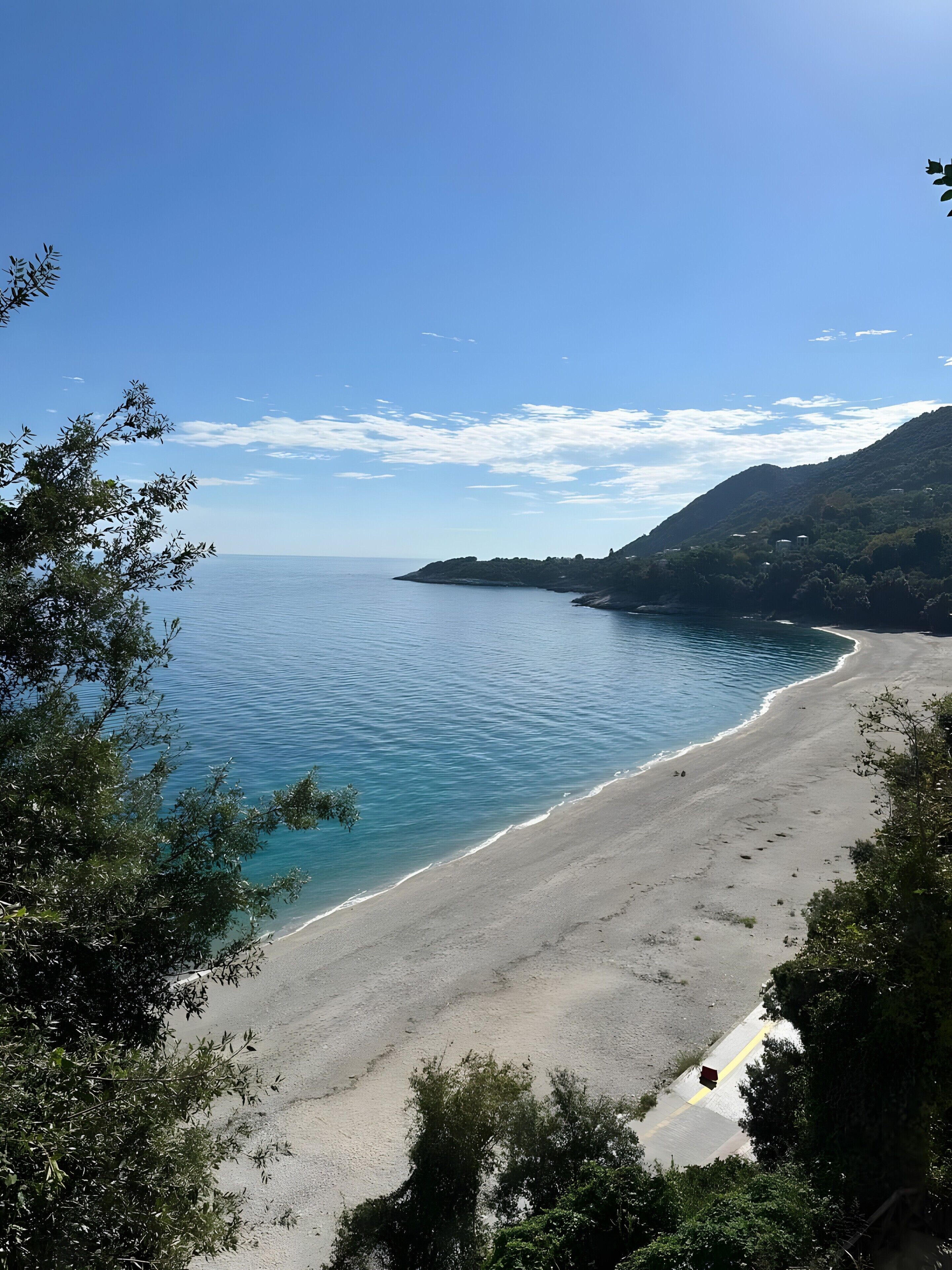Ein Strand mit klarem Wasser, einem Sandstrand und einer hügeligen Landschaft im Hintergrund.