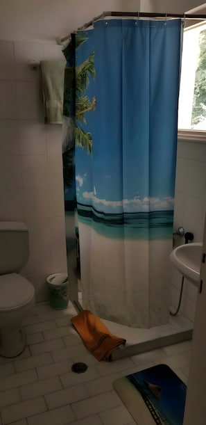 Ein Badezimmer mit Duschvorhang mit tropischem Motiv, Toilette, Waschbecken und Mülleimer.