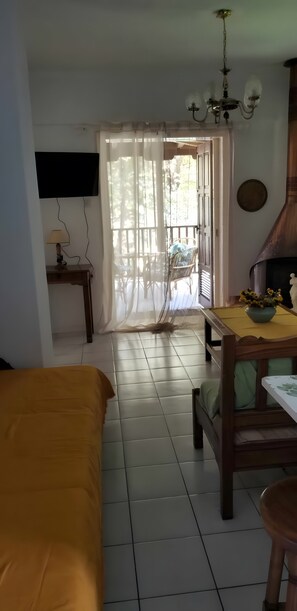 A room with a bed, a table with a bowl of flowers, a chair, a television mounted on the wall, and a fireplace.