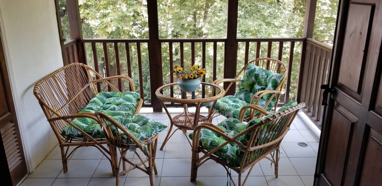 Een overdekt terras met rieten meubilair en een kleine tafel, omringd door een houten balustrade.