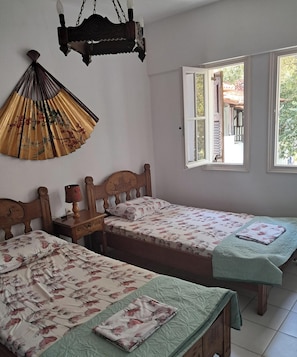 Ein Zimmer mit zwei Holzbetten, einem Deckenventilator und einem Fenster mit Blick nach draußen.