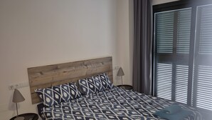 A bedroom with a bed, a bedside lamp, a window with blinds, and a wall socket.