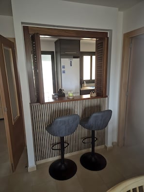 Una zona de bar con dos taburetes, un refrigerador y una ventana con persianas.