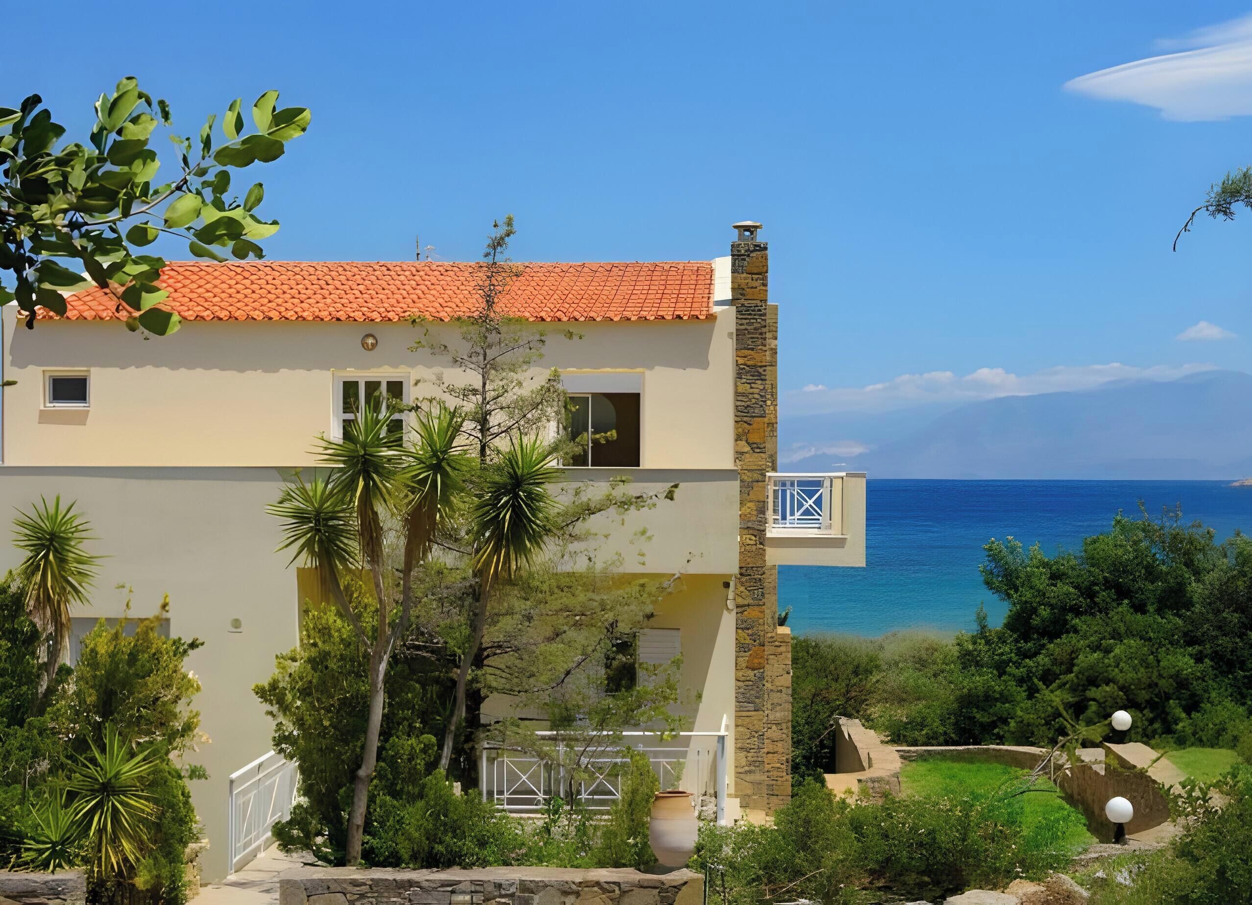 A two-story building with a red-tiled roof, a stone chimney, and a view of the sea.