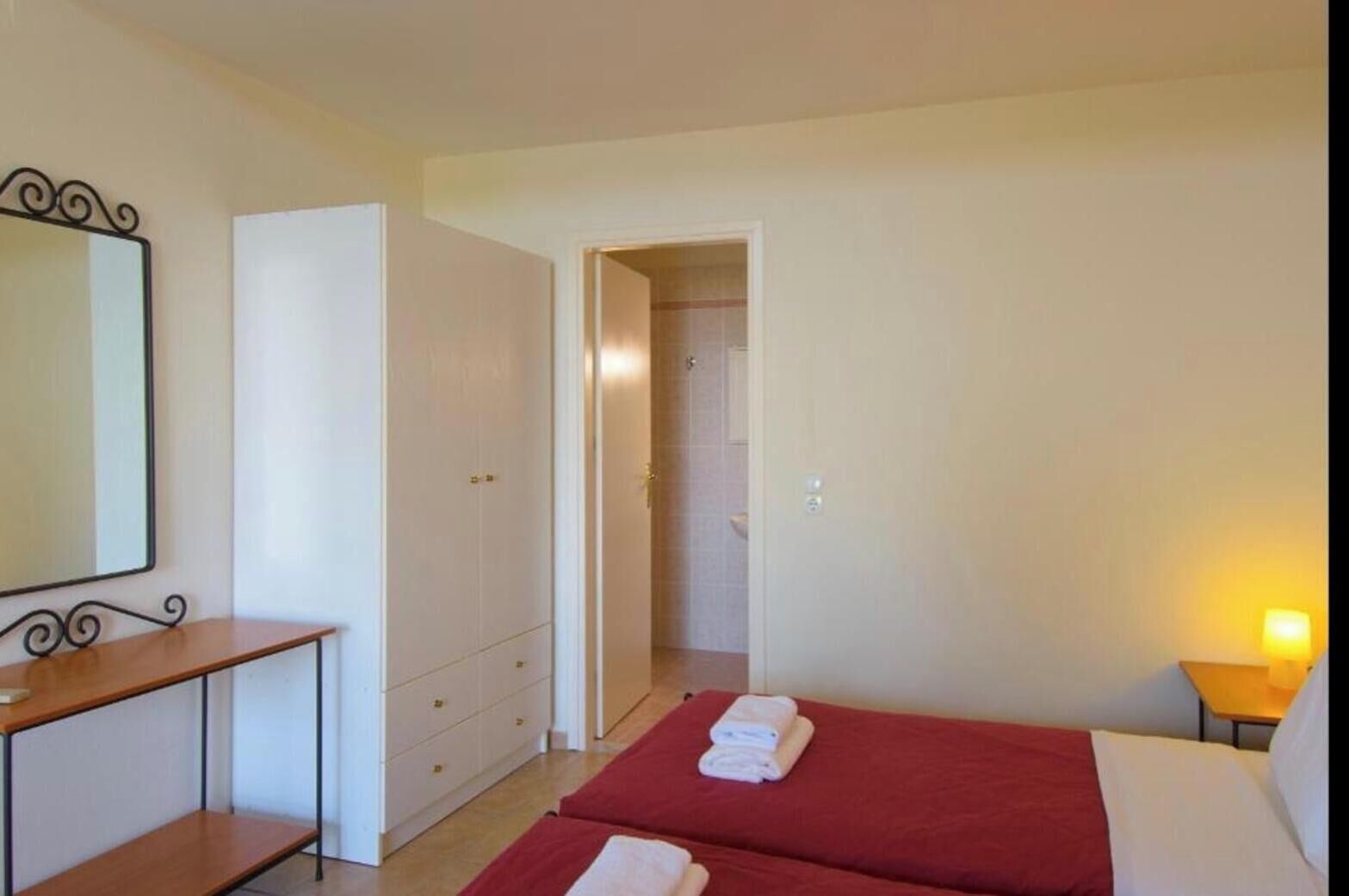 A hotel room with a bed, a desk, a wardrobe, and a bathroom visible through an open door.