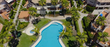 Vue aérienne d’un complexe hôtelier doté d’une grande piscine, entourée de palmiers et de pelouses bien entretenues.